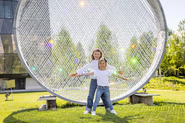 Twee kinderen in witte topjes voor een grote glinsterende cirkel. Buitenopname op een weiland bij zonnig weer.