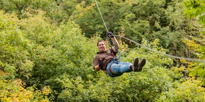 Ausflug mit Kindern - Weiler (Landkreis Mayen-Koblenz) - Ziplining bei EifelAdventures bedeutet, dass du entlang gespannter Stahlseile von Baum zu Baum gleitest, während du fest mit einem Gurtsystem verbunden bist. Die Zipline-Tour bei EifelAdventures ist nicht auf eine einzige Bahn begrenzt, sondern führt dich in Begleitung von professionell ausgebildeten Tour-Guides ca. 2,5 Stunden durch einen wundervollen Vulkaneifel-Wald. - Freizeitpark EifelAdventures