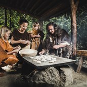 Ausflugsziel - Steinzeitfamilie beim Brotbacken im Ötzi-Dorf - Ötzi-Dorf und Greifvogelpark