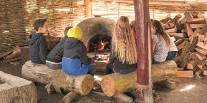 Viaggio con bambini - Großharras - Steinzeitdorf: Die eindrucksvolle Steinzeitsiedlung mit vielen Funden aus der Jungsteinzeit beinhaltet auch ein Kinderprogramm. An den „Wochenenden“ können sich die kleinen Besucher bei steinzeitlichen Tätigkeiten versuchen. Beim Töpfern, Steine Schleifen und Getreide Mahlen erleben die Kinder, wie die Menschen damals gelebt und gearbeitet haben. Wer möchte, kann auch beim Brot Backen zuschauen und das herrlich knuspriges Brot aus dem original steinzeitlichen Lehmofen probieren. - DER HELDENBERG